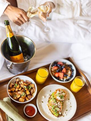 A cozy breakfast spread featuring champagne, colorful fruit bowls, a savory dish, and crispy potatoes, all served on a wooden tray.