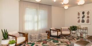 A cozy, modern lounge features stylish chairs, geometric-patterned rugs, greenery, and soft lighting, creating a welcoming atmosphere.