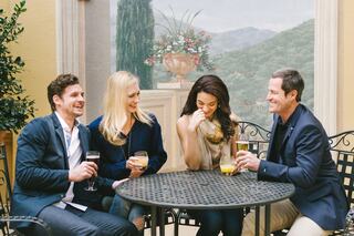 A group of four friends enjoys drinks together at a cozy outdoor table, laughing and sharing a joyful moment in a picturesque setting.