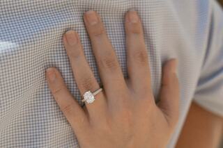 A hand rests gently on a shirt, showcasing a sparkling engagement ring with a floral design. Subtle and intimate moment captured.