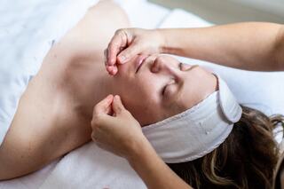 A woman receives a facial treatment, relaxing with her eyes closed while a therapist gently massages her face, enhancing her skincare routine.