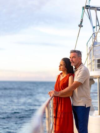 A couple enjoys a romantic moment on a boat, gazing out at the ocean under a colorful sky, radiating warmth and connection.