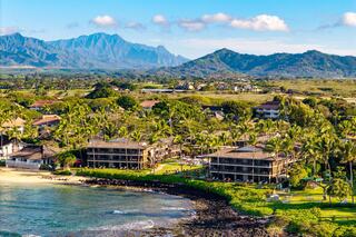 A scenic coastal view features lush greenery, palm trees, and serene ocean waters framed by majestic mountains in the background.