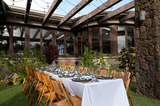 A beautifully set outdoor dining table with tropical greenery, elegant dishes, and string lights, creating a welcoming atmosphere.