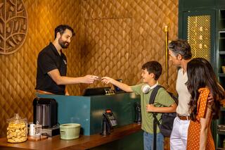 A boy hands a card to a friendly receptionist at a hotel, while his parents look on, creating a warm family check-in moment.