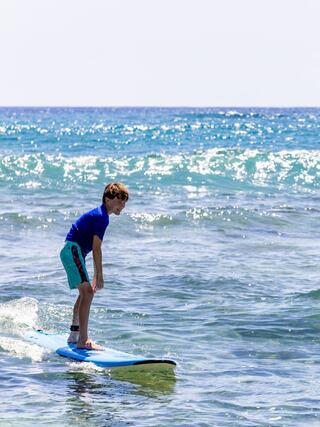 A young boy balances on a surfboard in the shimmering ocean, enjoying the thrill of riding small waves on a sunny day.