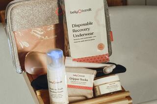 A collection of postpartum recovery essentials, including disposable underwear, skincare products, and gripper socks, neatly arranged in a basket.