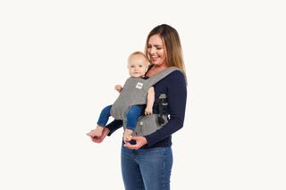 A woman in a navy top carries a baby in a gray carrier, both smiling, creating a warm and joyful parent-child moment.