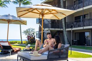 A couple enjoys drinks under umbrellas by a poolside, with a scenic view of the ocean and tropical surroundings. Relaxation and sun await.