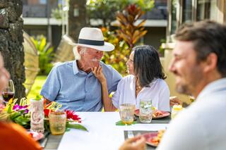 A joyful gathering features a smiling couple sharing a tender moment, surrounded by friends and vibrant tropical decor.