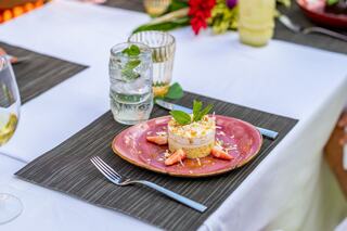 A cheerful group of friends enjoys a festive outdoor meal, raising glasses in a lush garden by a pool, surrounded by vibrant flowers.
