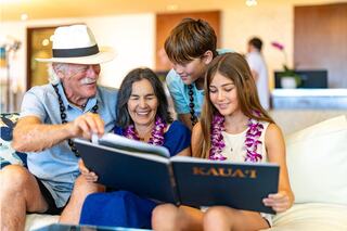 A cheerful family reviews a photo book together, wearing leis and enjoying quality time in a bright, modern setting.