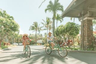 A couple enjoys a sunny bike ride through a tropical landscape, surrounded by palm trees and vibrant greenery. Fun and carefree atmosphere.