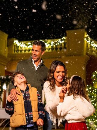 A joyful family enjoys a snowy evening outdoors, sharing laughter and warmth amidst festive decorations and twinkling lights.