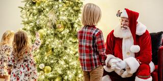 A cozy holiday scene with a decorated Christmas tree, as two children interact with Santa Claus in festive attire.