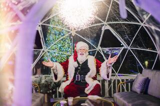 A cheerful Santa Claus in a festive igloo, surrounded by holiday decorations, warmly welcoming guests with open arms.