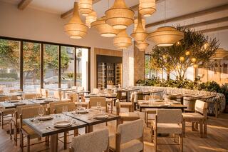 A stylish dining area featuring modern wooden furniture, woven pendant lights, and large windows, creating a warm and inviting atmosphere.