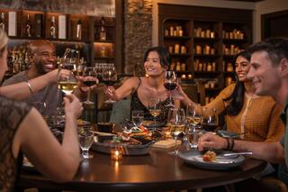 Friends joyfully toast at a dinner table filled with food and drinks, celebrating together in a warm, inviting ambiance.