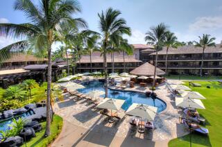 A tropical resort features a shimmering pool surrounded by palm trees, lounge chairs, and shaded areas, inviting relaxation and leisure.