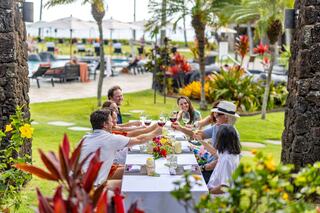 A cheerful group toasts at an outdoor table surrounded by lush greenery and vibrant flowers, enjoying a festive gathering.