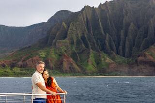 A couple embraces on a boat, surrounded by lush green cliffs and calm waters, enjoying a serene moment in a stunning natural landscape.