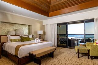A stylish hotel room features a king-size bed, modern decor, and a balcony with ocean views, complemented by cozy seating.