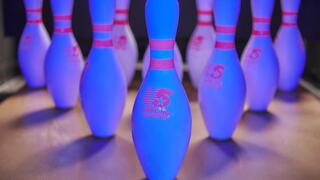 Brightly lit bowling pins with blue illumination, featuring pink stripes and a logo, set up in a lane, ready for a game.