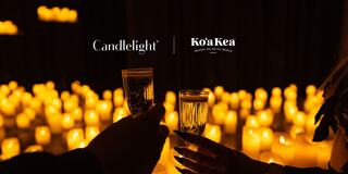 Two glasses are raised in a toast, surrounded by a warm glow of candlelight, creating an intimate and celebratory atmosphere.