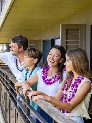 A cheerful family enjoys time together on a balcony, wearing leis and sharing smiles, capturing a joyful and relaxed moment.