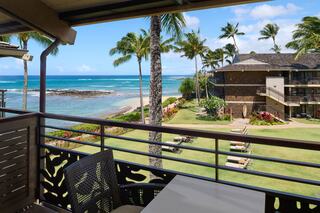 A peaceful ocean view from a balcony, featuring palm trees, a lush lawn, and a charming beachfront property under a clear blue sky.