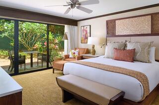 A stylish hotel room features a king-sized bed, seating area, and large glass doors opening to a lush outdoor view.