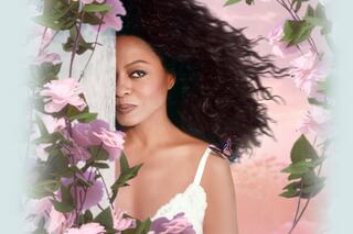 A woman with curly hair peeks from behind a post, adorned with flowers, a butterfly resting on her shoulder against a soft, pastel background.