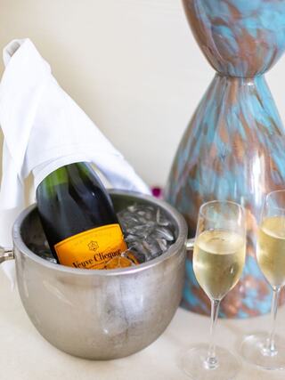 A bottle of Veuve Clicquot champagne rests in a silver ice bucket, accompanied by elegant flutes and a decorative vase.